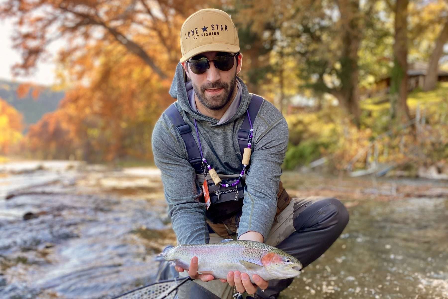 Angler holding a rainbow trout in the Guadalupe River below Canyon Dam during fall color
